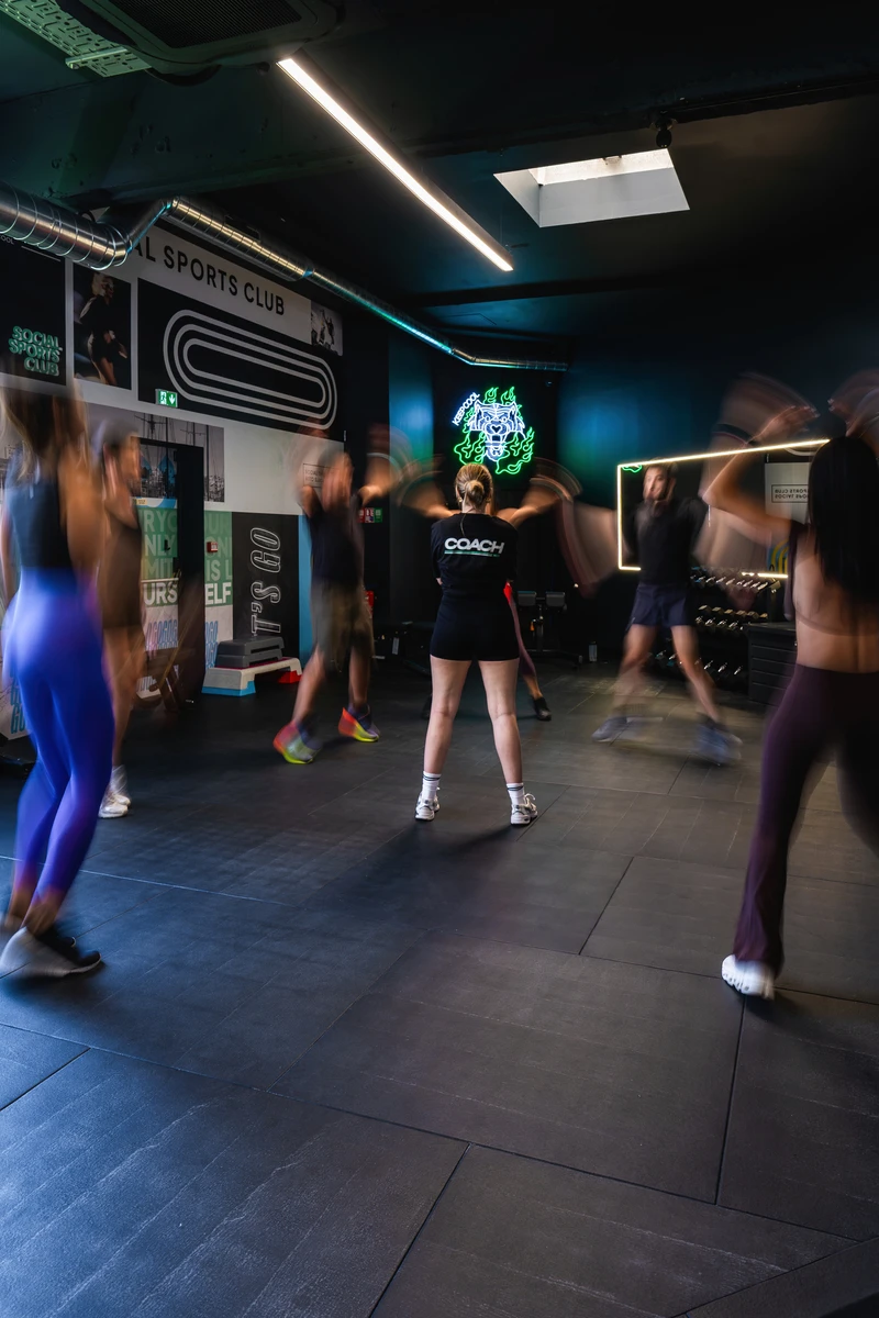 Coach leading a group workout in a gym with participants doing jumping jacks in motion blur.