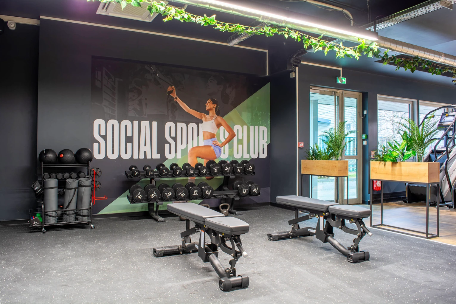 Salle Keepcool Bourgès avec équipements musculation : bancs de développé couché, rack poids libres, mur végétal et logo Social Sport Club.