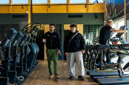 Salle de sport Keepcool avec équipements cardio et musculation, deux personnes en discussion devant machines.
