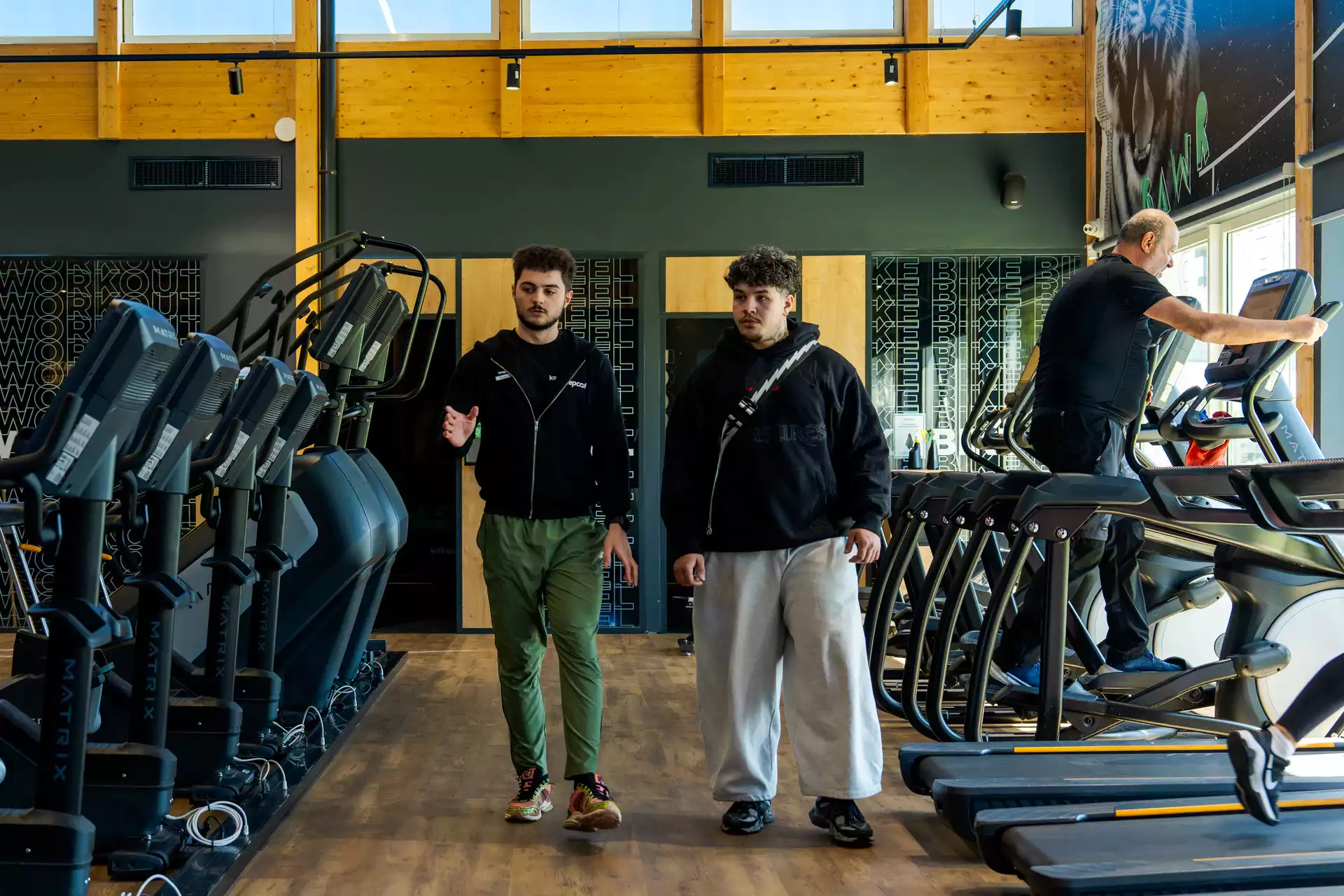 Salle de sport Keepcool avec équipements cardio et musculation, deux personnes en discussion devant machines.