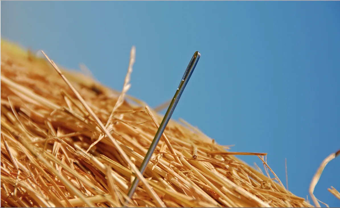 A sewing needle standing upright in a haystack against a clear blue sky