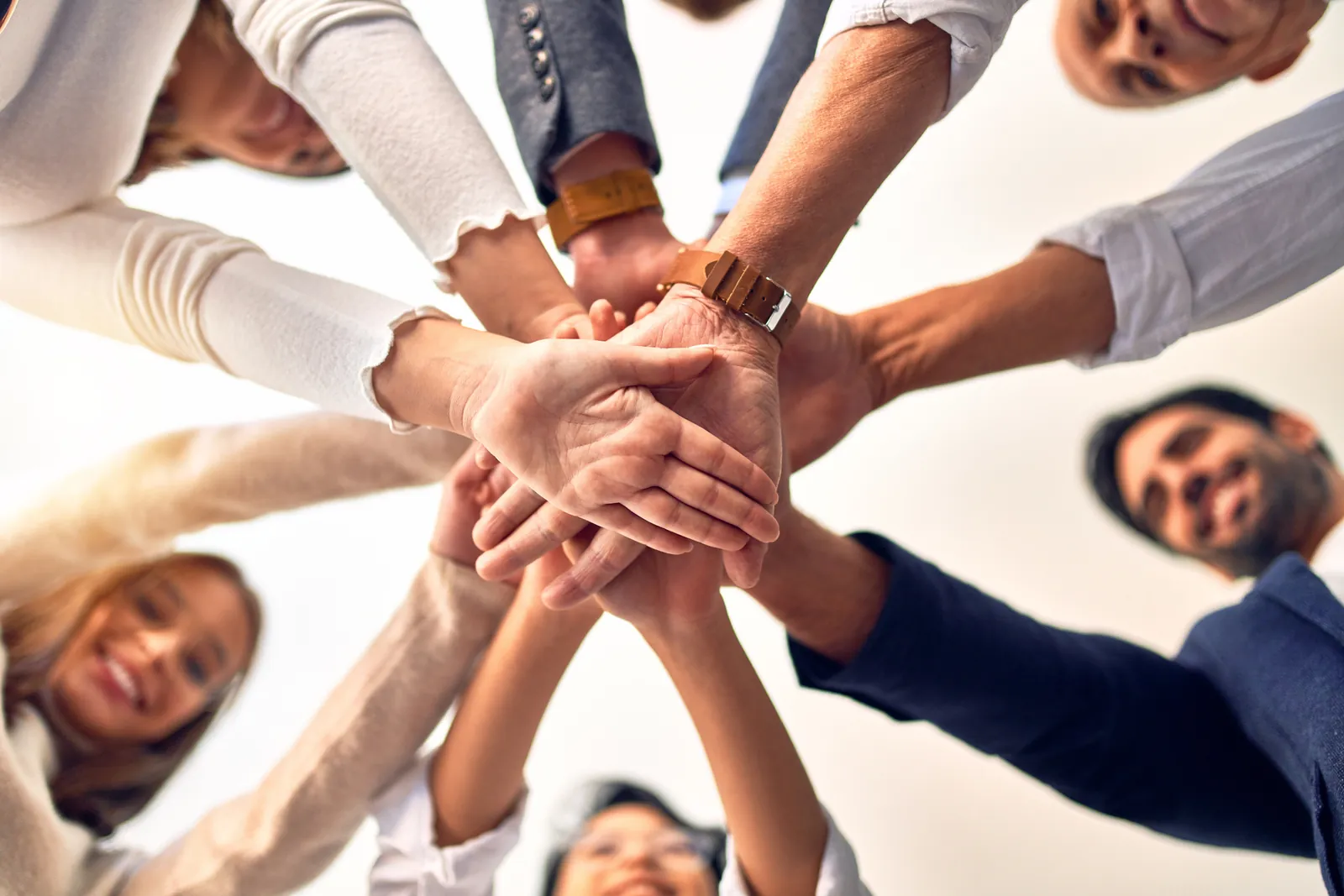 A team of colleagues seen from below, stacking their hands together in the centre of a circle