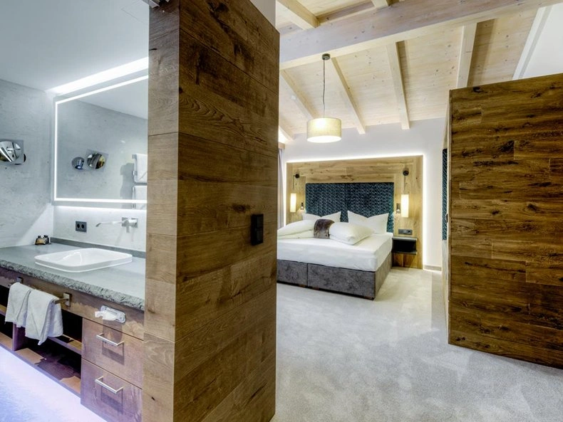 Hotel Strass open-plan suite with timber wall partitions, exposed beam ceiling, and modern bathroom.