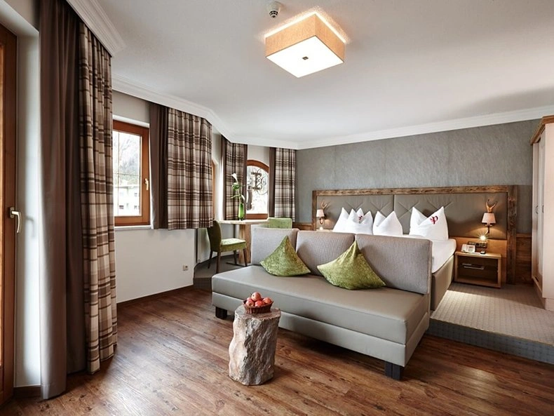 Hotel Strass room with a grey sofa, green cushions, plaid curtains, and warm wooden flooring.