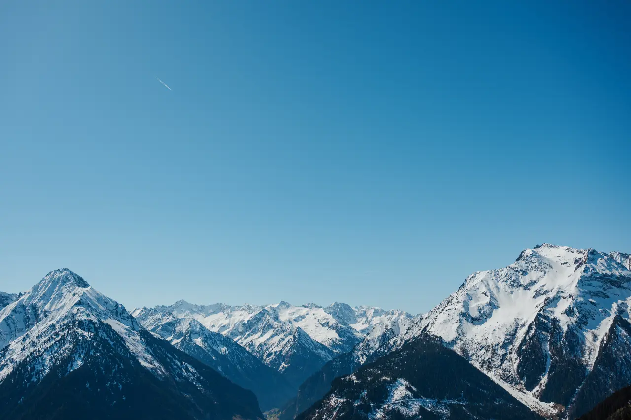 Snow-covered mountain peaks under a clear blue sky with a faint airplane trail.