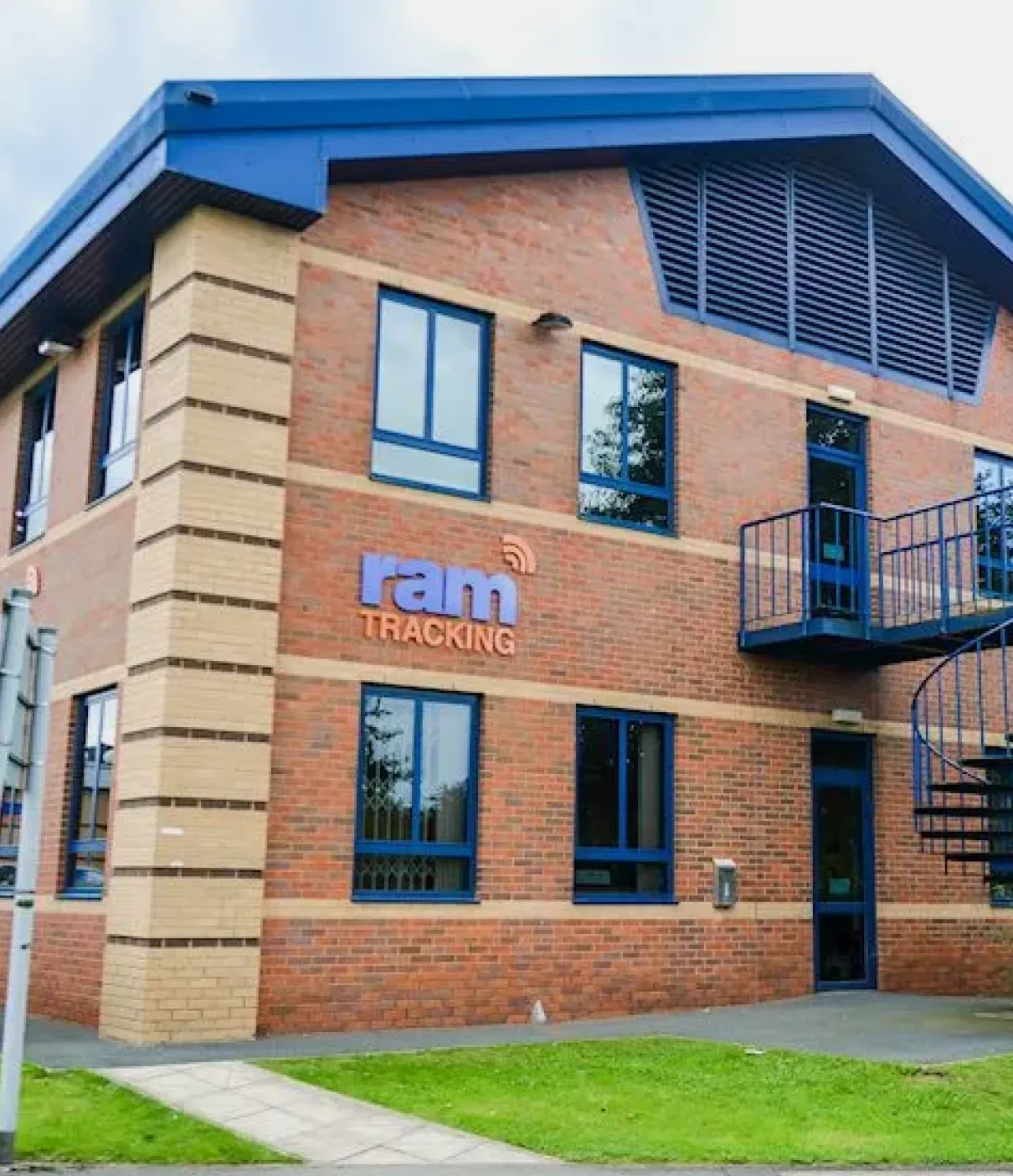 Two-story brick office building with blue window frames and a spiral staircase, displaying the ram TRACKING logo on the wall.