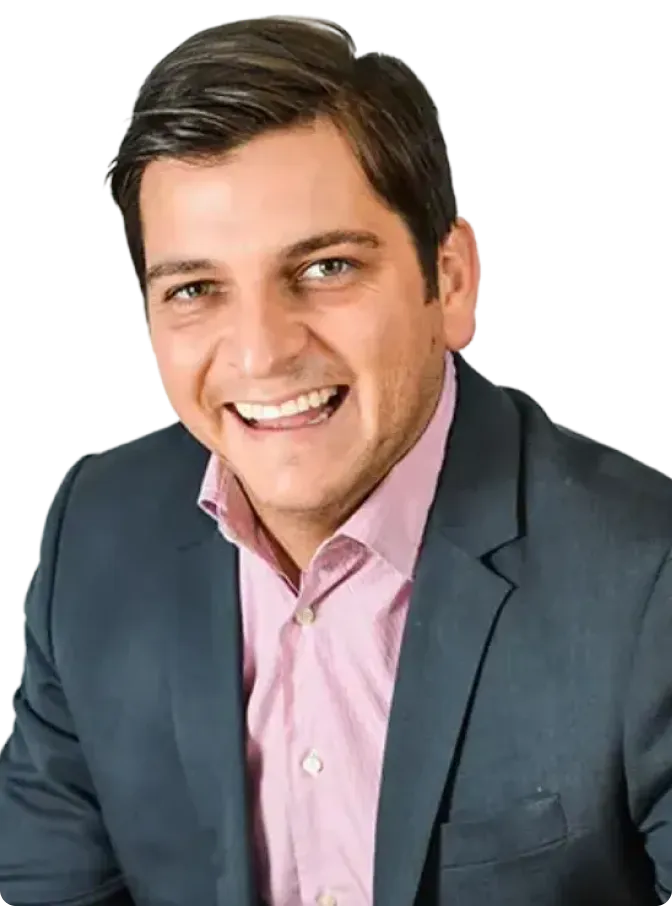 Smiling man with dark hair wearing a navy blazer and light pink button-up shirt.