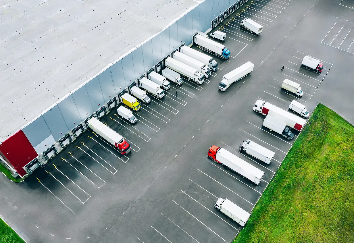 Aerial view of a warehouse loading dock with several semi-trailer trucks and smaller delivery trucks parked and positioned for loading and unloading.