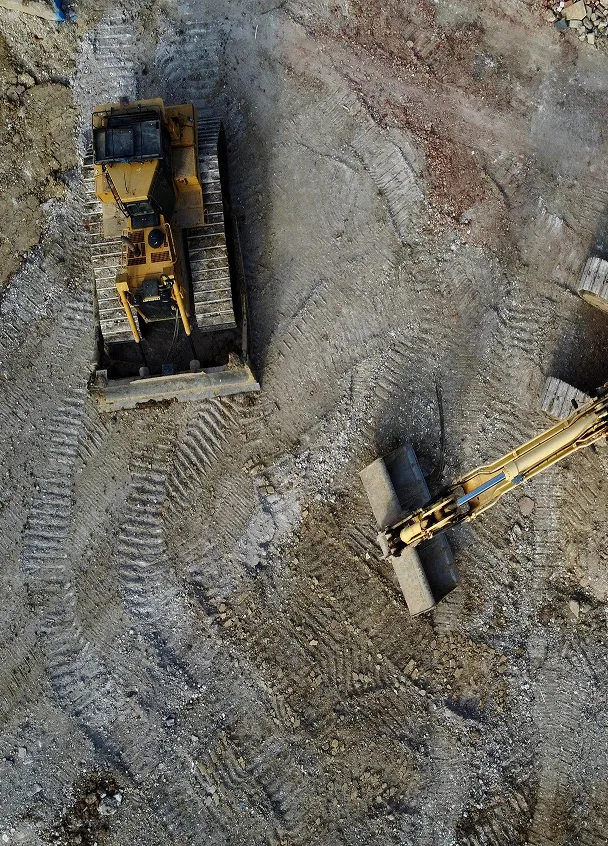 Aerial view of two yellow construction bulldozers on a dirt and gravel construction site with visible tire tracks.