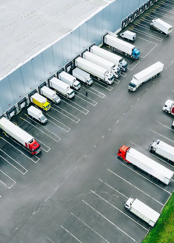 Aerial view of multiple semi-trucks parked in loading bays of a large warehouse.