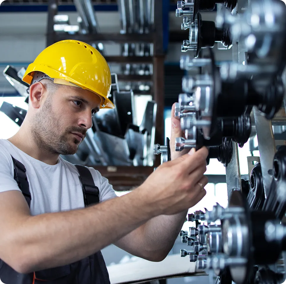 Industrial worker wearing a yellow hard hat inspecting machinery with bolts in a factory setting.