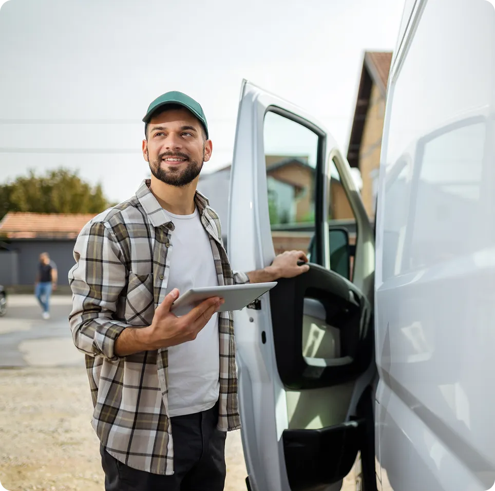 Smiling delivery man holding a tablet and opening the door of a white van outdoors.