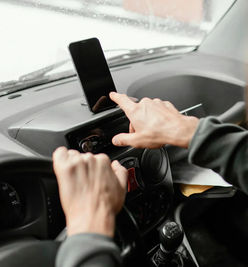 Person touching a smartphone mounted on a car dashboard while holding the steering wheel with the other hand.