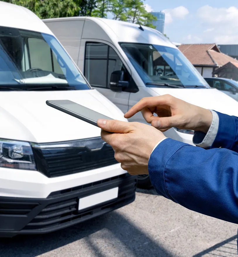 Person in blue jacket using a tablet in front of white commercial vans parked outside.