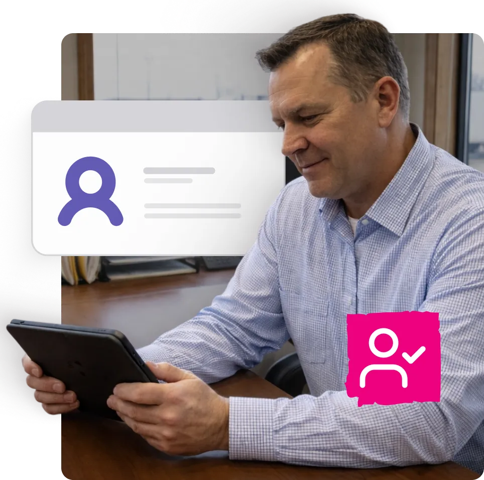 Man in a checkered shirt sitting at a desk, looking at a tablet, with digital icons of user profiles floating beside him.