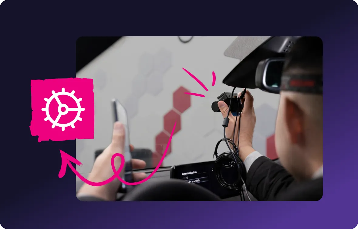 Person inside a car holding a dash cam near the rearview mirror with a steering wheel icon and arrow pointing to the camera.