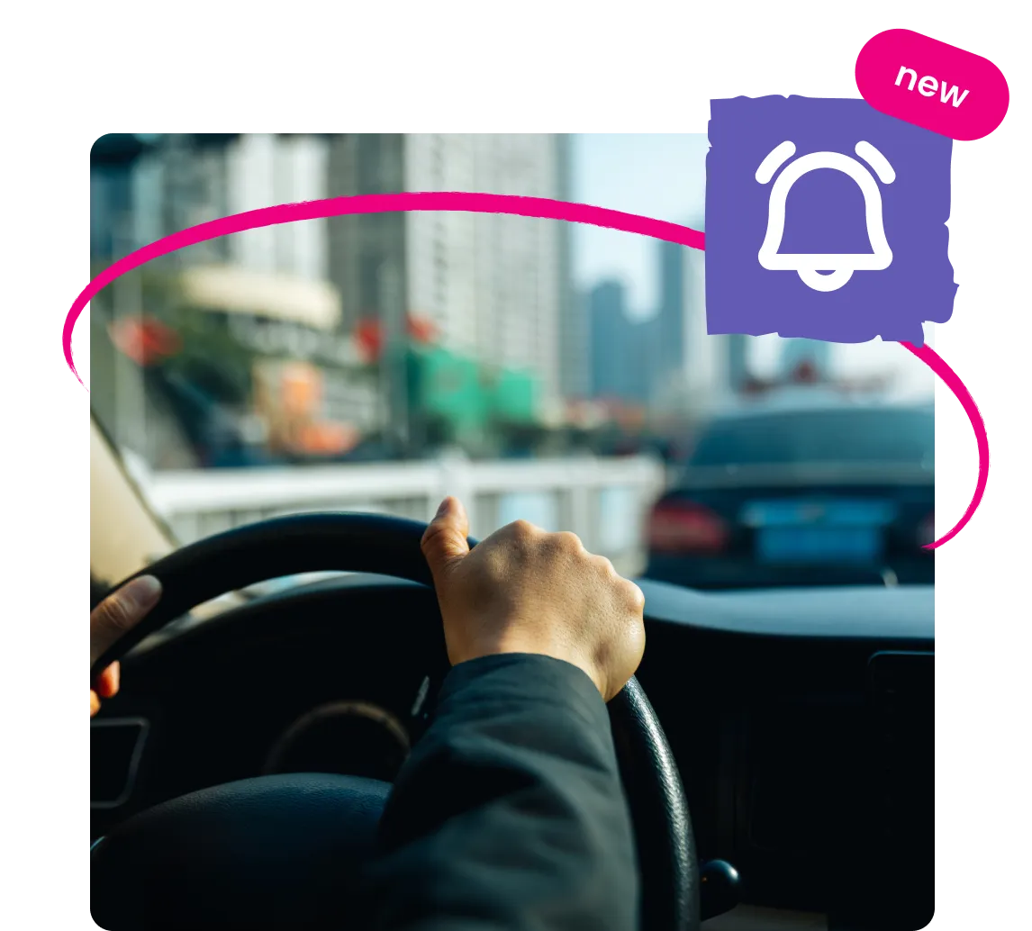 Driver holding steering wheel inside car with alert bell icon and 'new' label, city traffic visible outside.