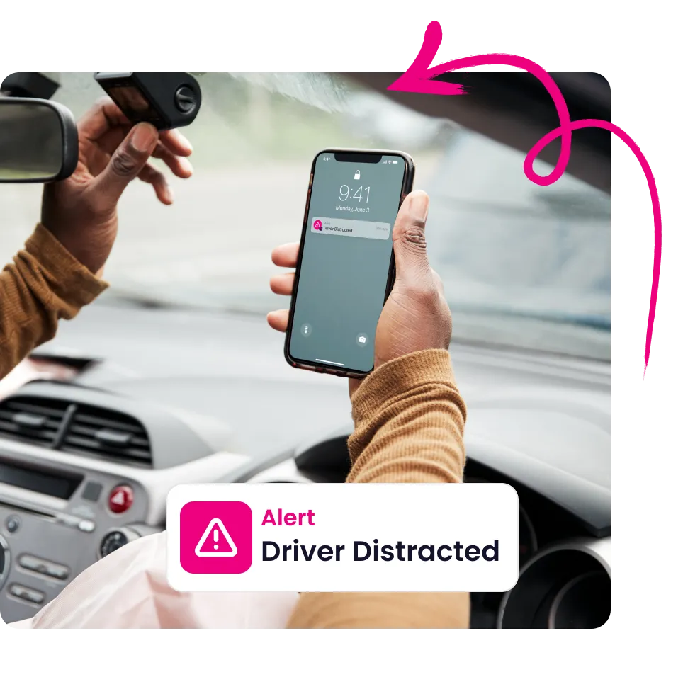 Person holding a phone showing an alert notification that reads 'Driver Distracted' inside a car with a dashcam mounted on the windshield.