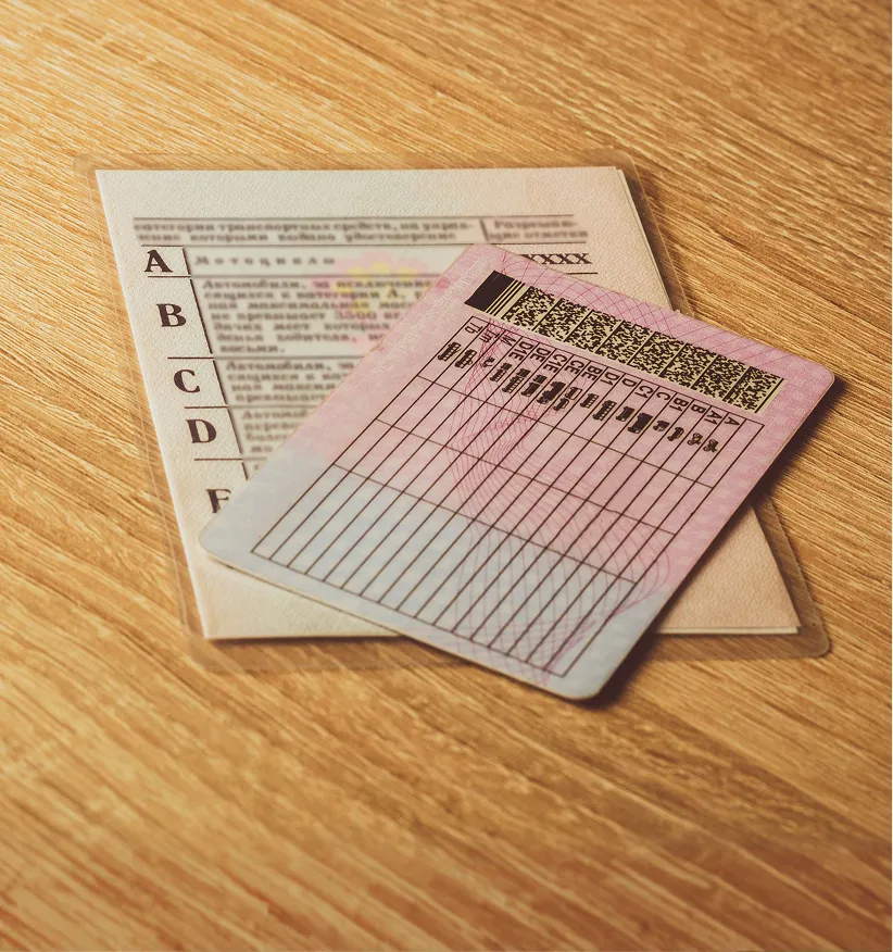 Two laminated cards on a wooden surface, one with a list of vehicle categories labeled A to F in Cyrillic script, and the other with rows and columns of data and a barcode at the top.