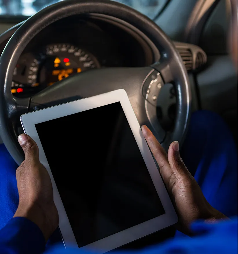 Driver holding a tablet at the steering wheel of a vehicle