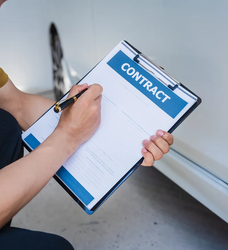 Person signing a contract on a clipboard beside a white vehicle.