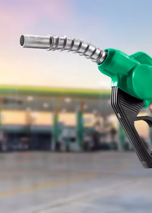 Person holding a fuel pump with a petrol station in the background