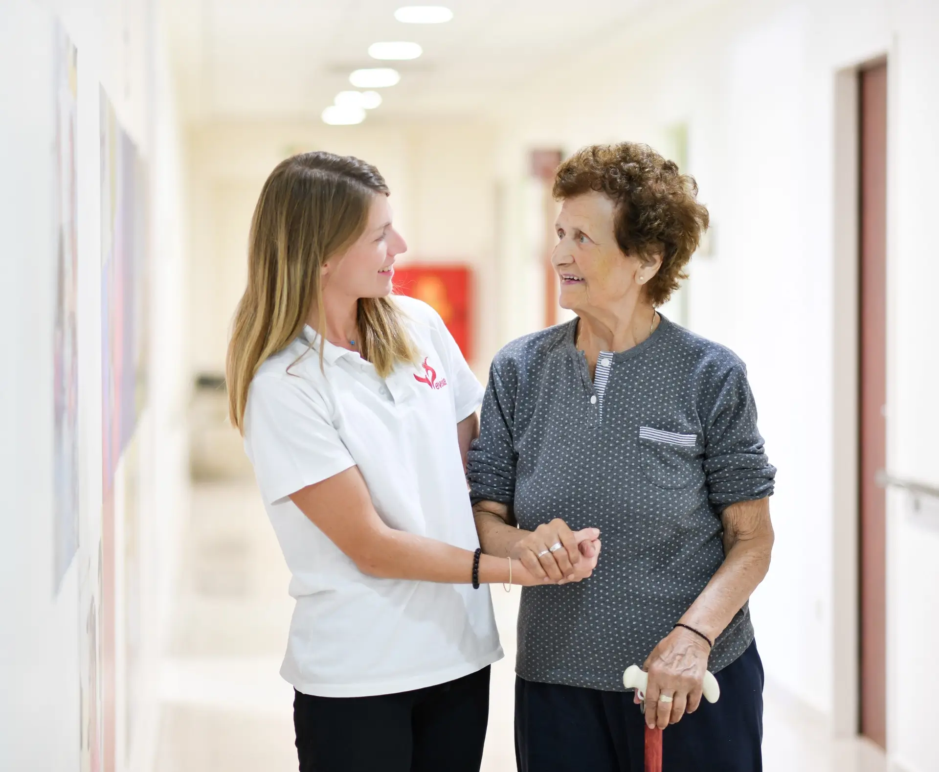 Therapist holding hands with an older woman walking with a cane in the corridor