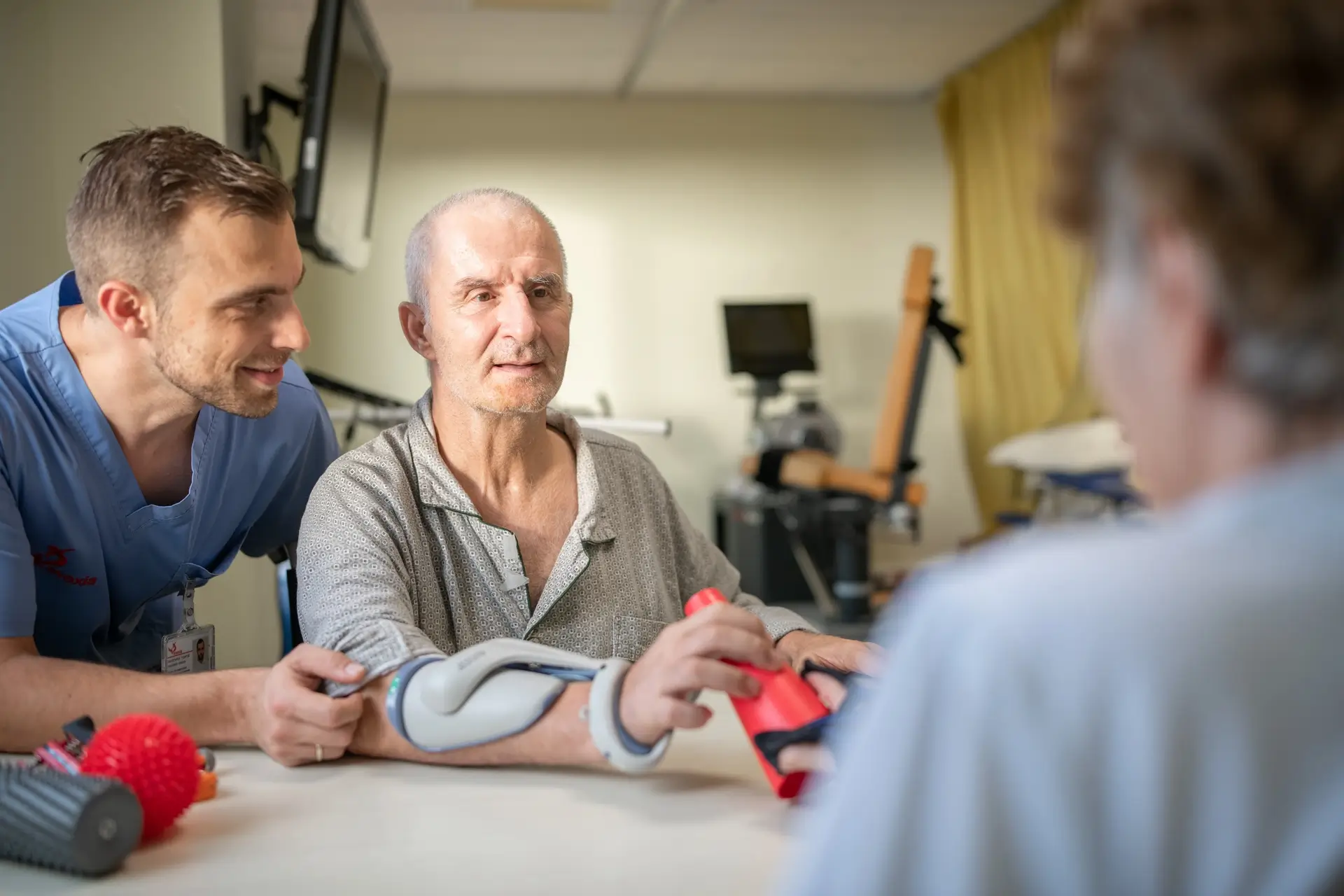 Elderly man with arm brace doing hand exercise with therapist in rehabilitation room.