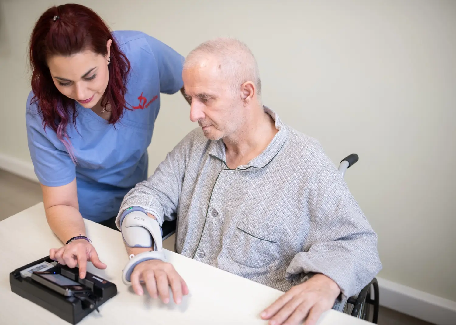 Therapist in blue scrubs supporting a man's braced arm during a hand function assessment at a table