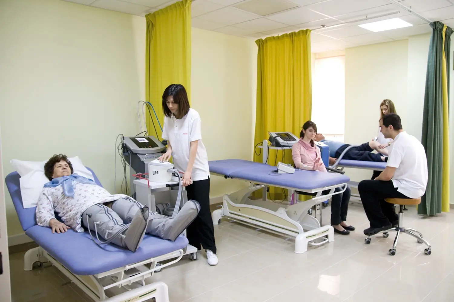 Patients receiving compression therapy on treatment beds while staff members monitor the equipment