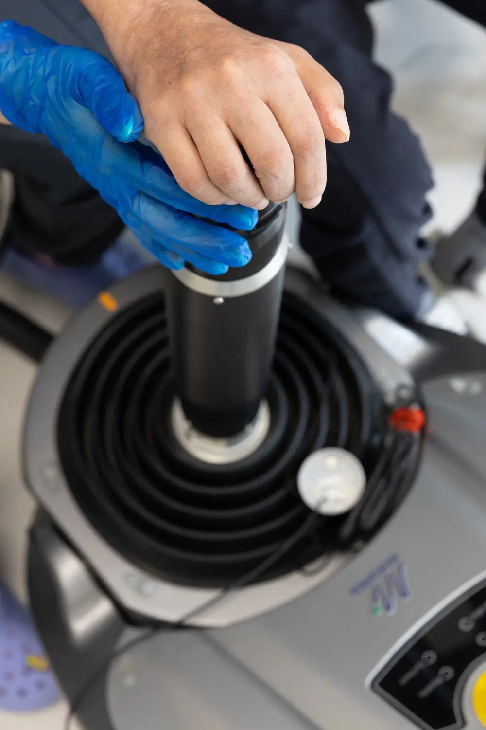 Gloved clinician's hand lifting a treatment applicator from its coiled-cable holder on a therapy machine