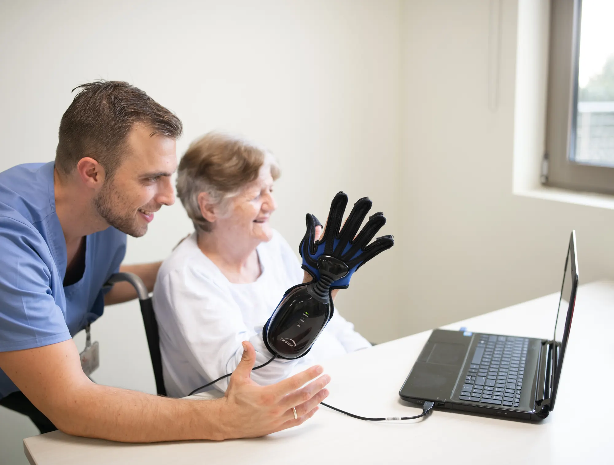 Older woman laughing as she works a robotic rehabilitation glove with her therapist
