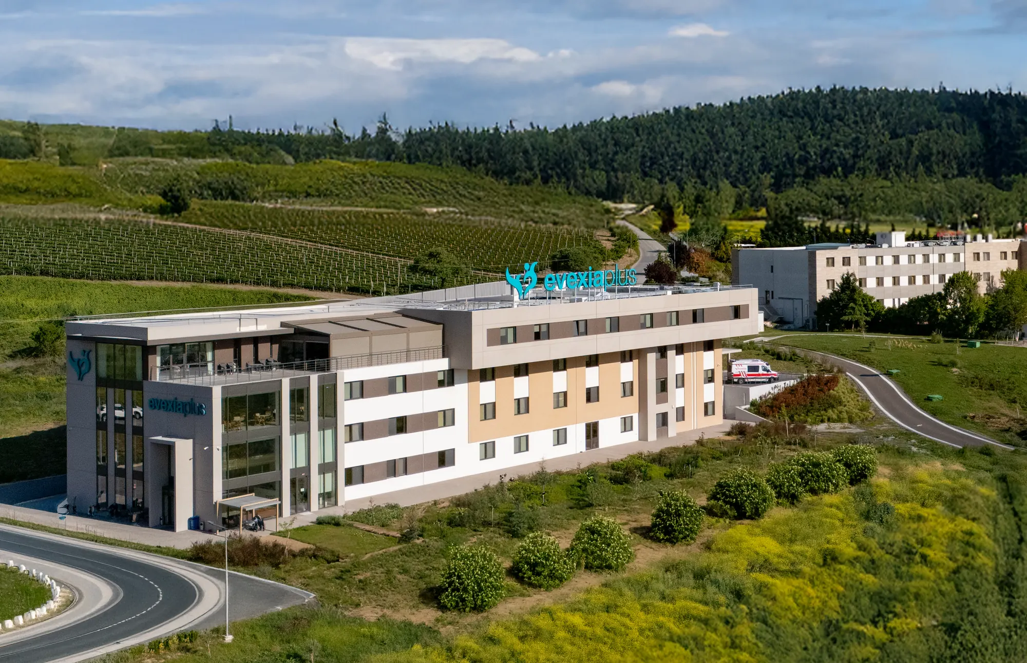 Aerial view of the Evexia Plus building on a hillside surrounded by fields