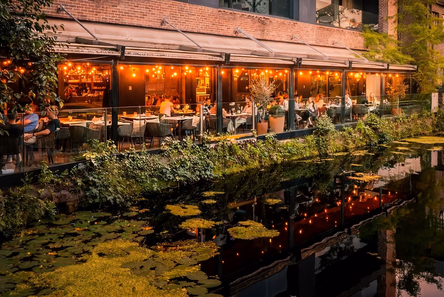 Upscale restaurant interior with red leather booths, glass pendant lights, and greenery on walls.