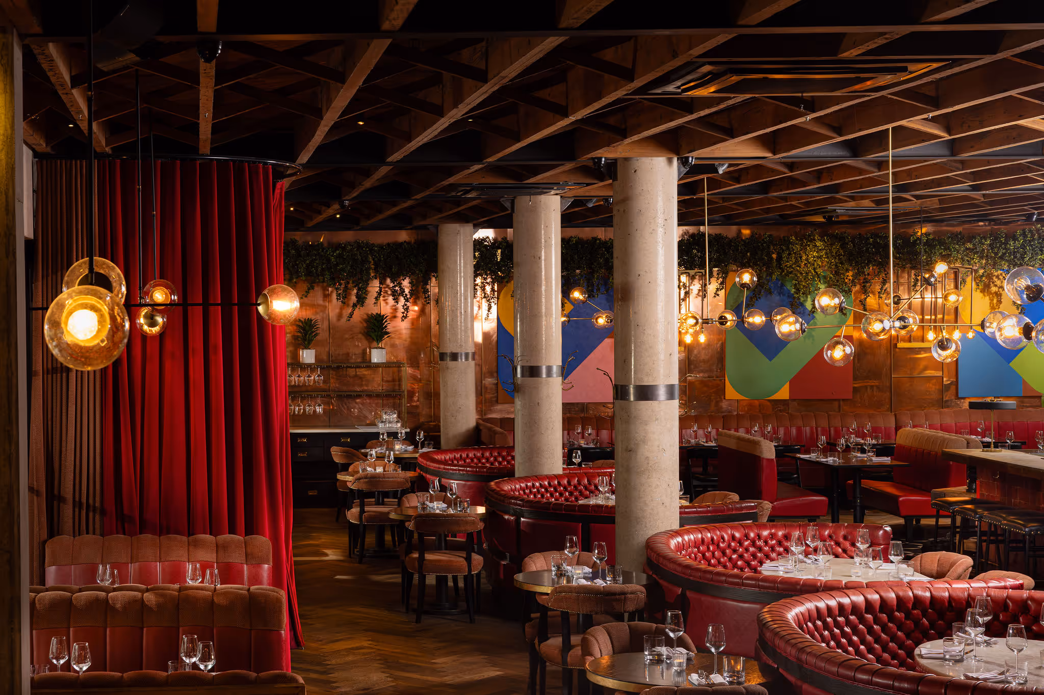 Upscale restaurant interior with red leather booths, glass pendant lights, and greenery on walls.