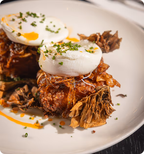 Two poached eggs garnished with chives on crispy fried food with mushrooms on a white plate.