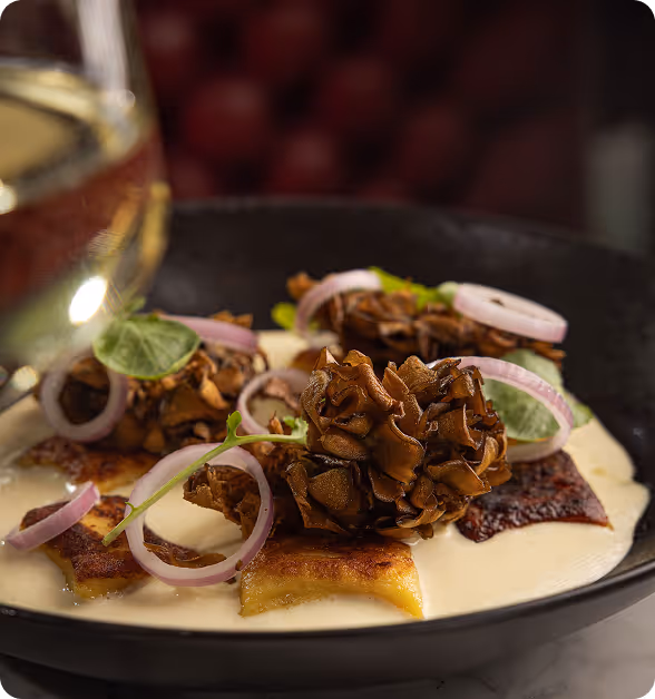 Creamy sauce with browned gnocchi topped with sautéed mushrooms, red onion rings, and fresh herbs in a black bowl.
