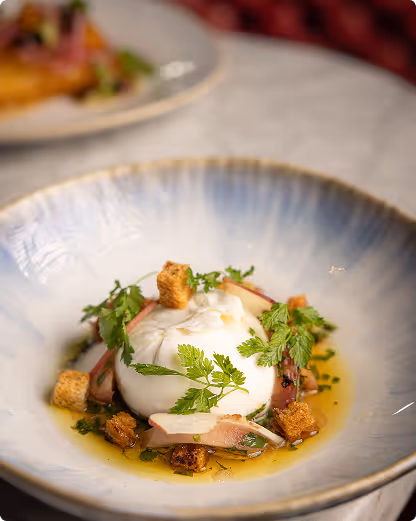 Gourmet dish with poached egg, croutons, herbs, and sauce in a gray-blue ceramic bowl.