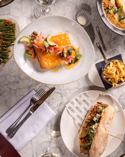 Table with plated cooked fish topped with vegetables, sandwich, fries, and asparagus side dish.