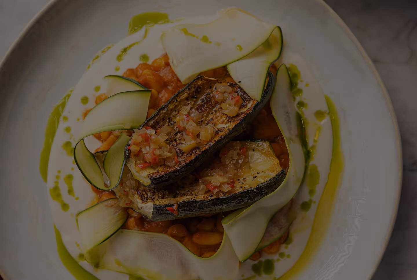 Grilled zucchini halves with diced topping served on beans and thin zucchini ribbons with green sauce drizzle.