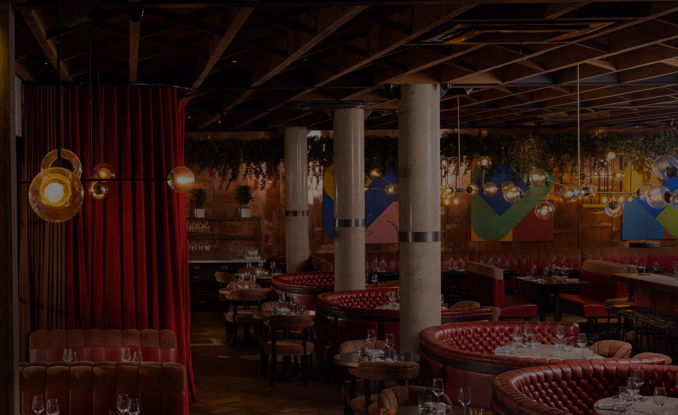 Elegant restaurant interior with red leather banquettes, round tables, modern lighting, and colorful wall art.