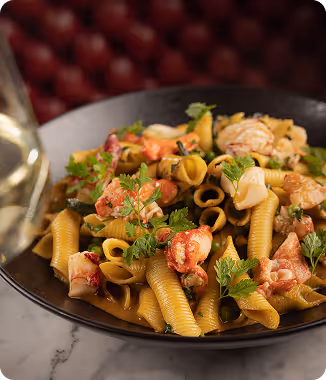 Pasta with chunks of lobster and garnished with fresh herbs on a black plate.