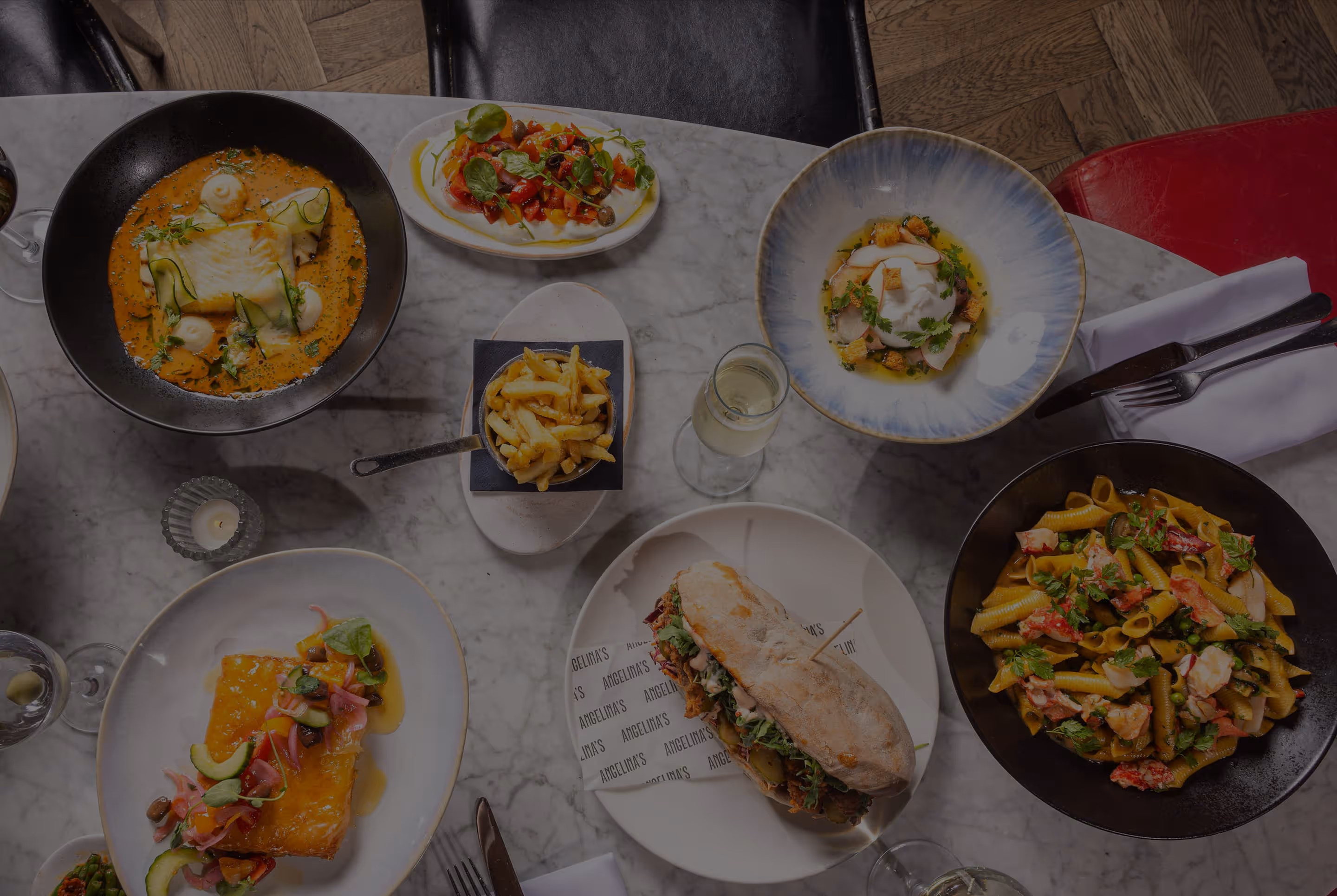Table with diverse gourmet dishes: sandwich, pasta, fries, fish, salad, and a creamy poached egg dish.