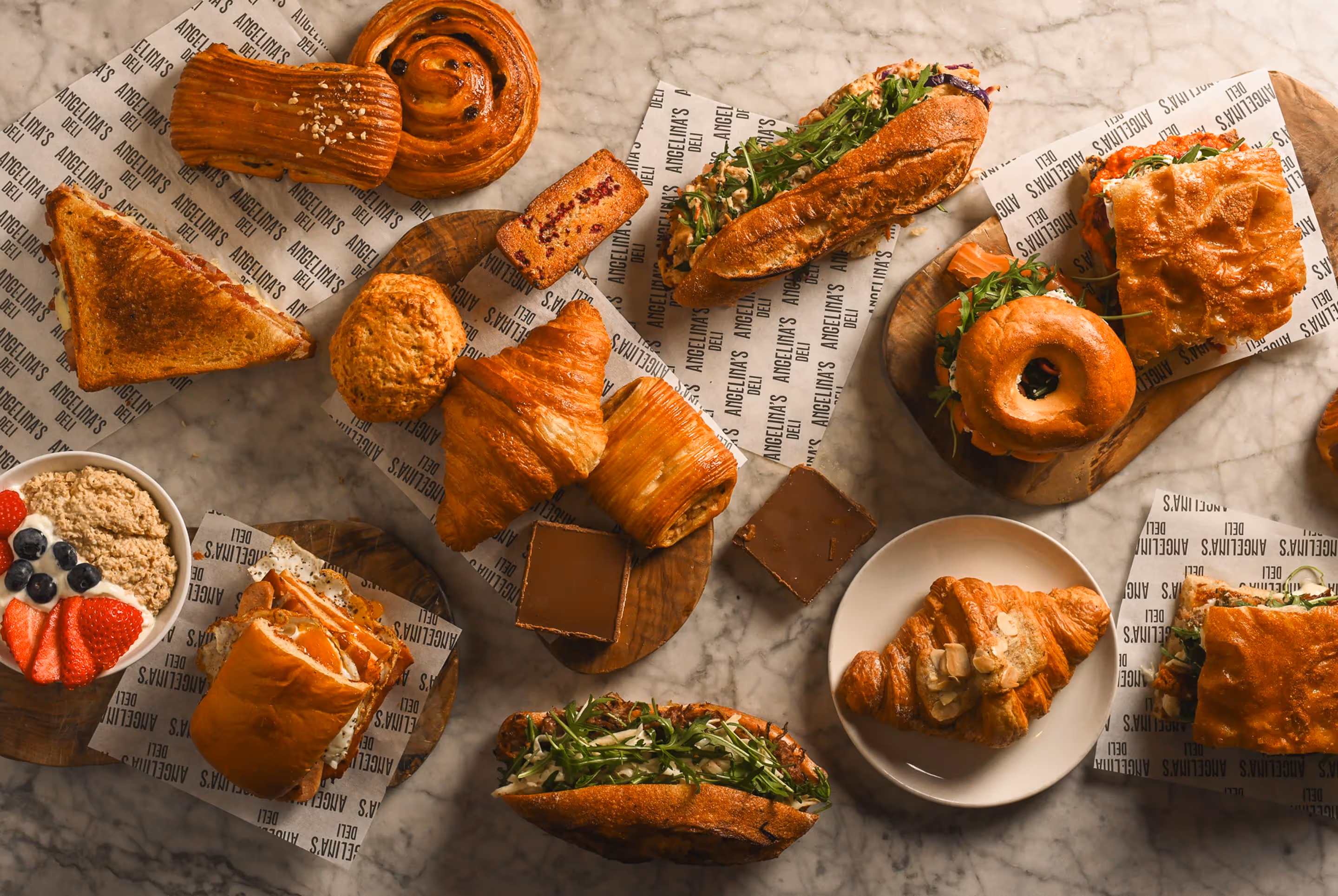 Variety of sandwiches, pastries, and desserts arranged on a marble table with branded paper.