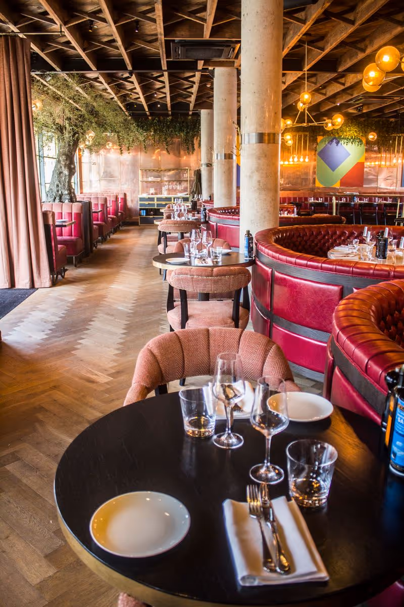 Upscale restaurant interior with red leather booths, round tables set with glasses and plates.
