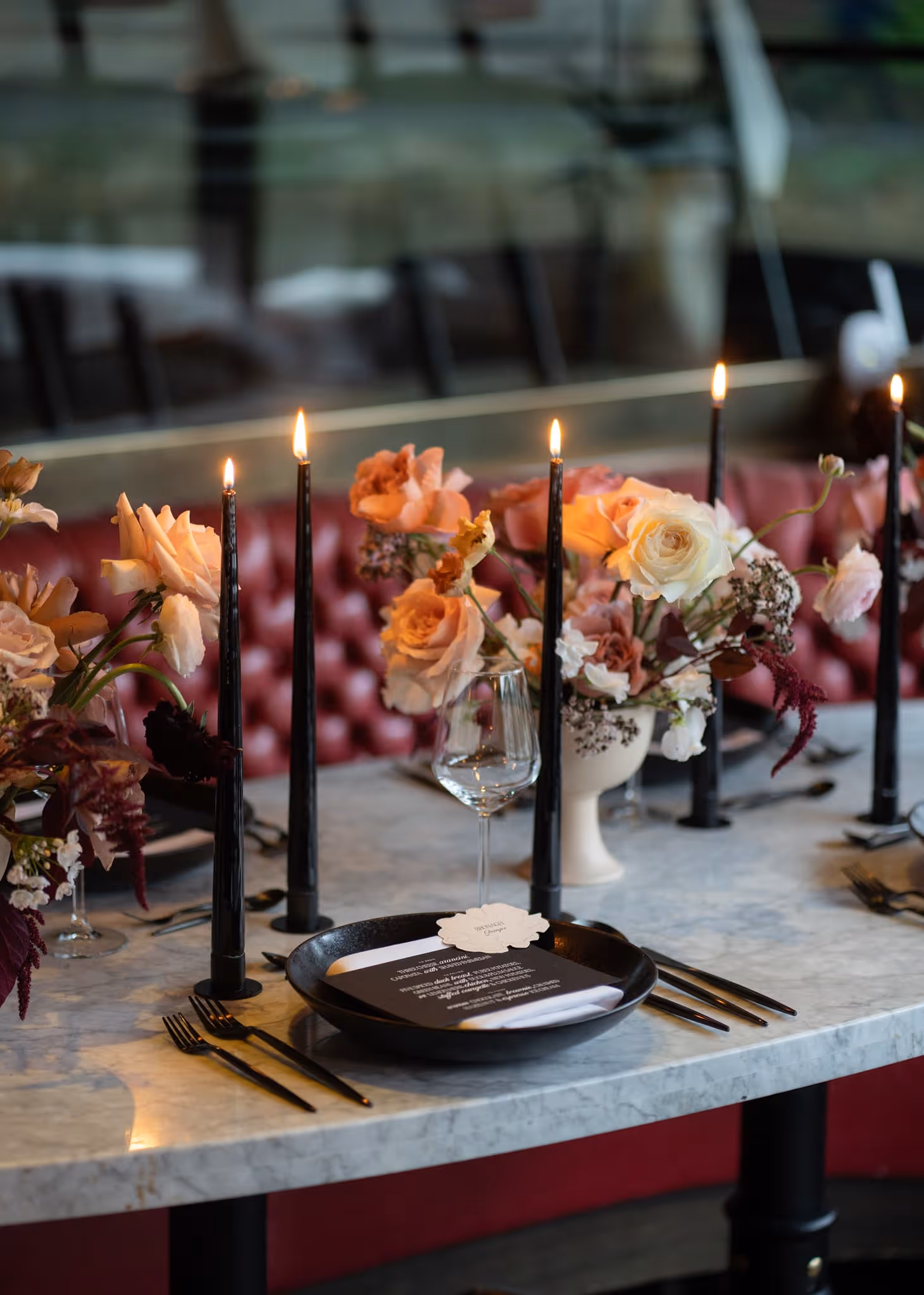 Table with black candles, floral arrangements, black plate and silverware set for a formal dinner.