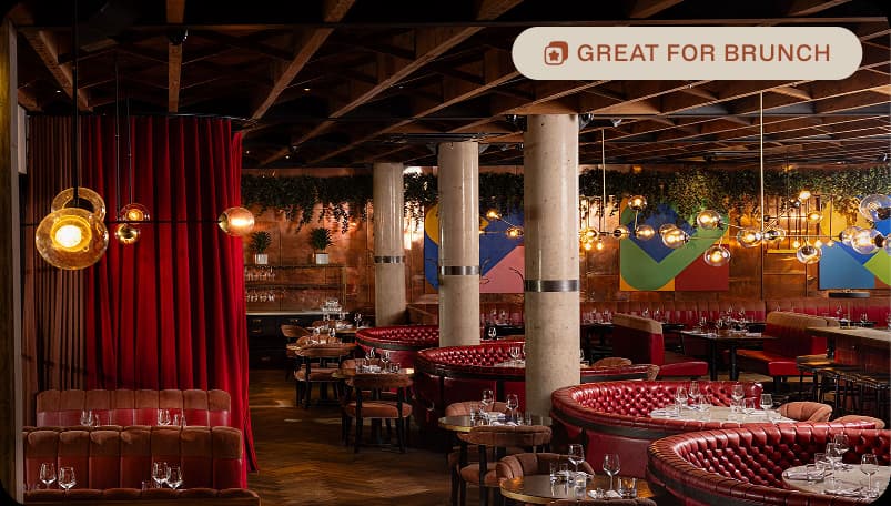 Stylish restaurant interior with red booths, round tables, hanging lights, and modern art on walls.