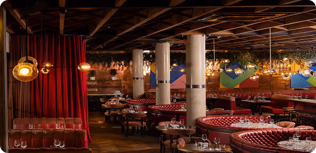 Stylish restaurant interior with red booths, round tables, hanging lights, and modern art on walls.