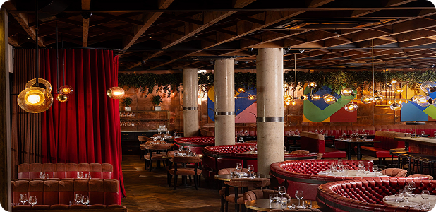 Stylish restaurant interior with red booths, round tables, hanging lights, and modern art on walls.