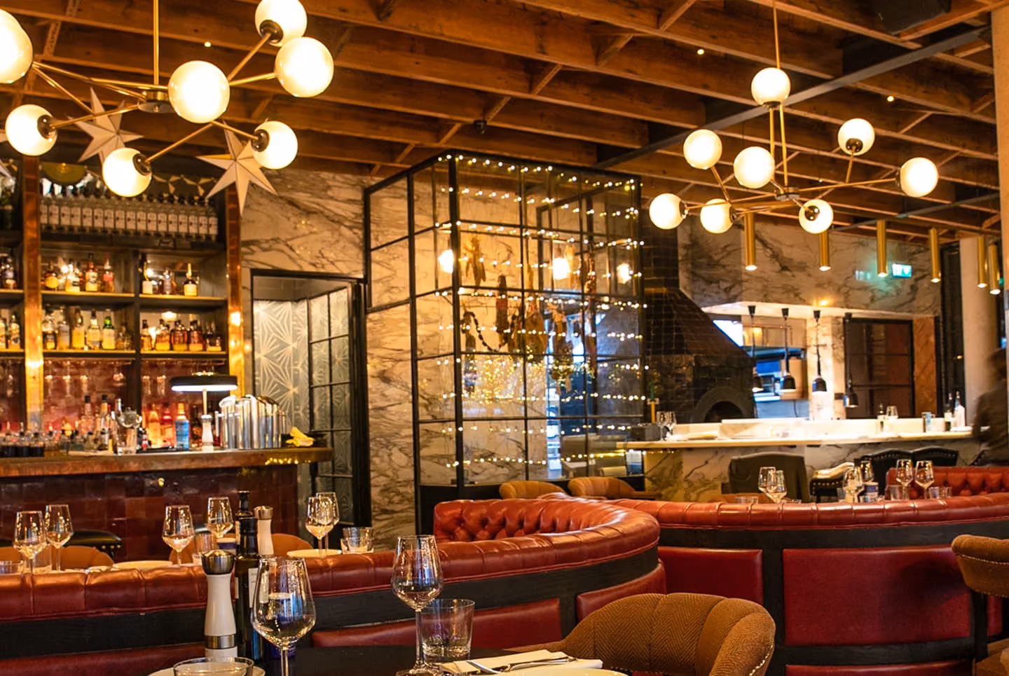 Cozy modern restaurant interior with red leather booths, marble walls, a stocked bar, and warm lighting.